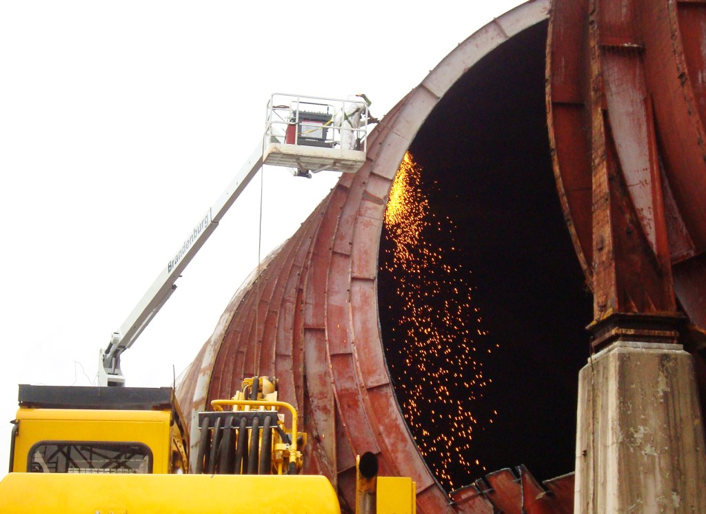 Man in lift with torch cutting tunnel shell