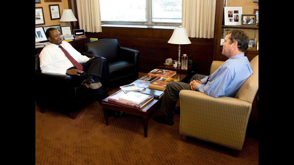 Two men seated in chairs in office.