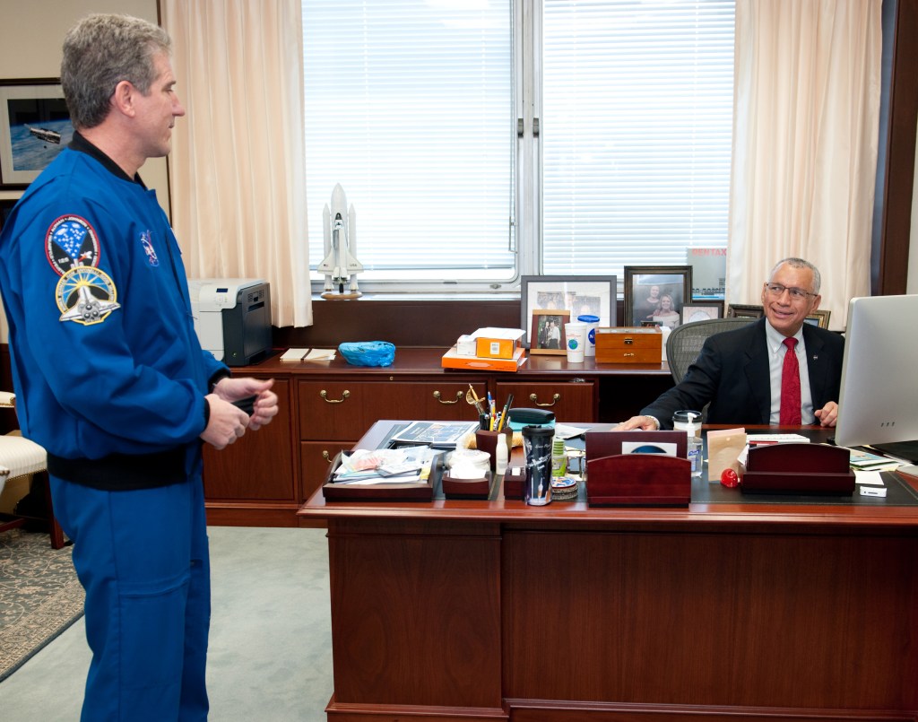 Astronaut and man seated at desk.