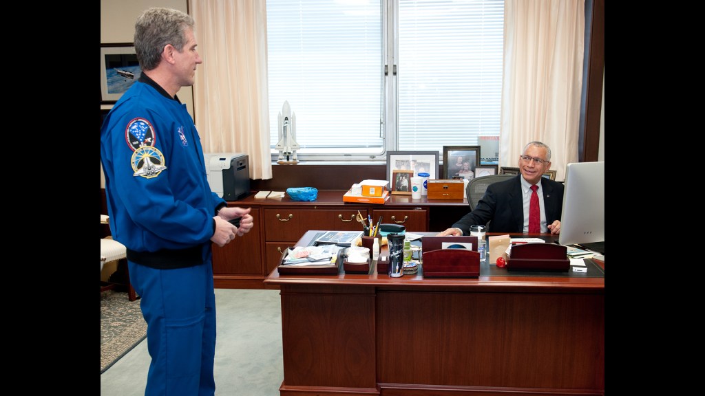 Astronaut and man seated at desk.
