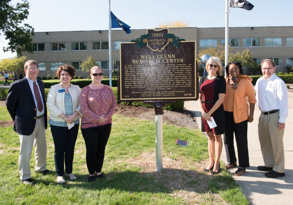People standing around sign in front of building.