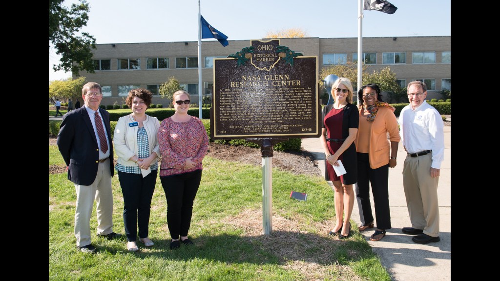 People standing around sign in front of building.