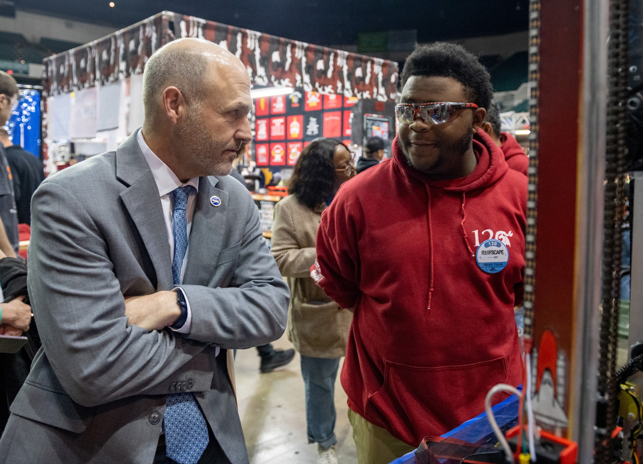 Standing in the work area where robots are adjusted for competition, NASA Glenn’s center director and a FIRST Robotics participant casually discuss robotics and the competition.