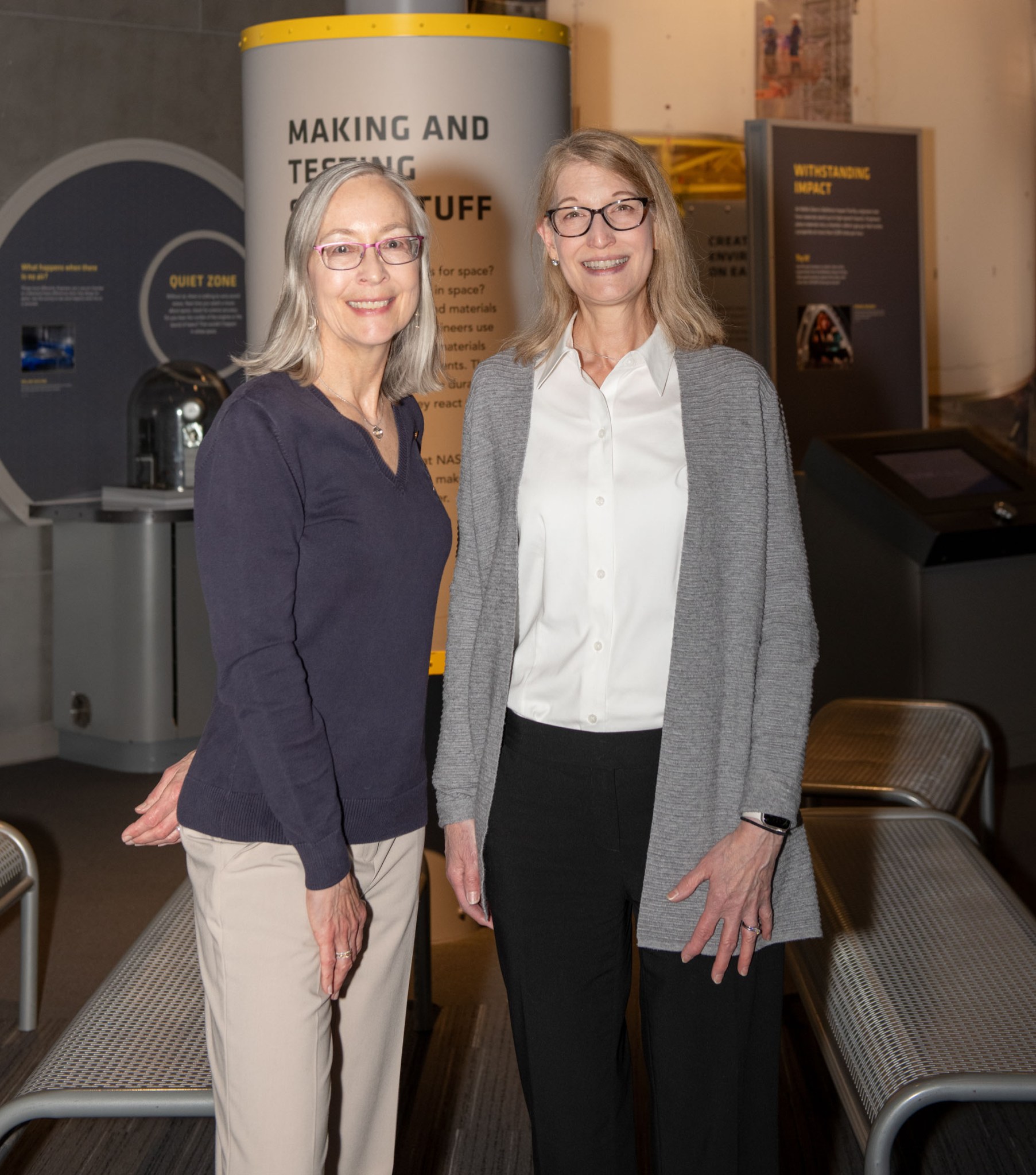 Glenn Visitor Center, in Cleveland on Thursday, May 8, 2025. Alt Text: NASA research engineers Kim de Groh, left, and Joyce Dever, pose for a photo with various interactive displays behind them at NASA Glenn Research Center’s Visitor Center.