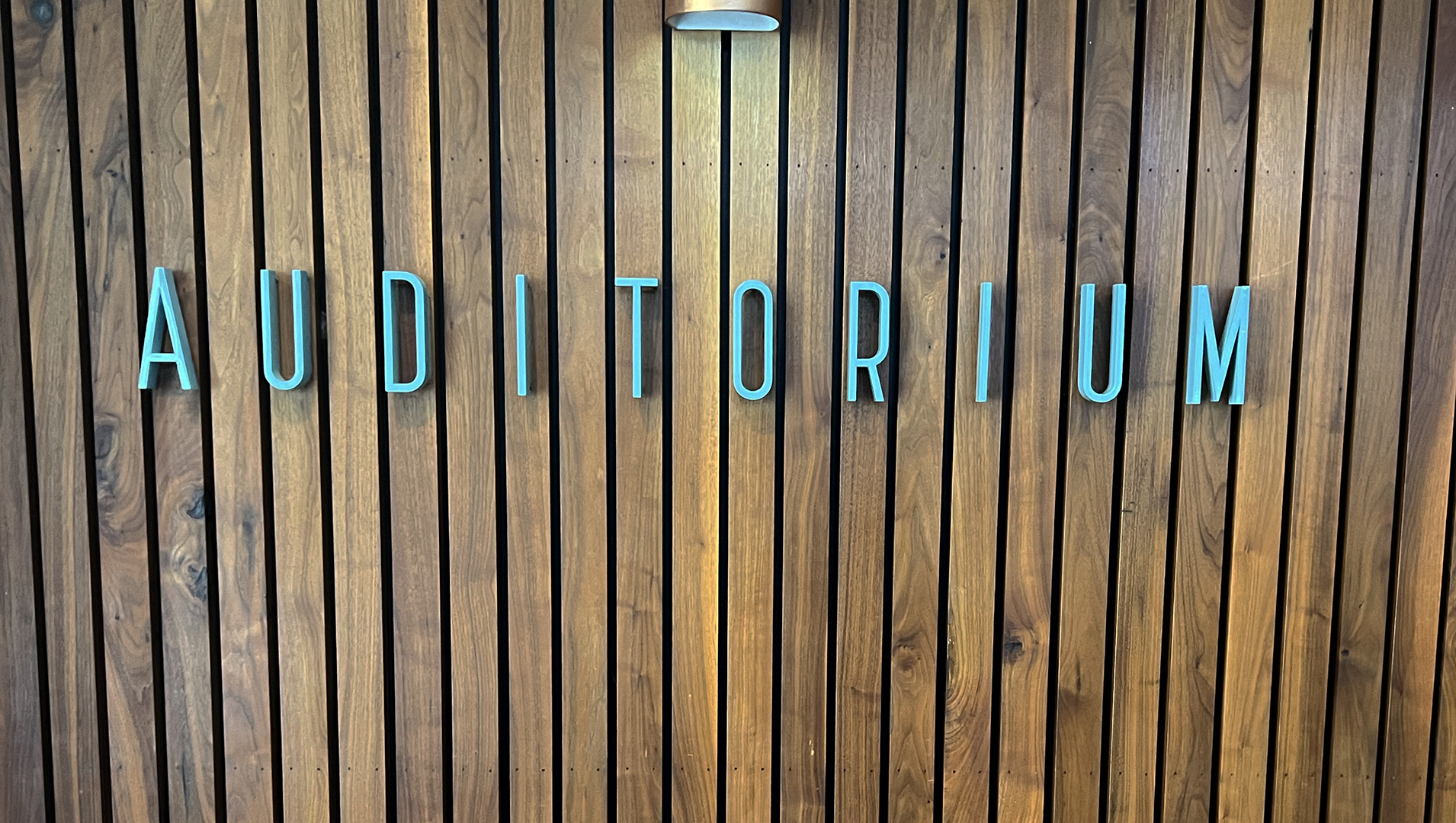 Blue letters spelling "Auditorium" on wood wall.