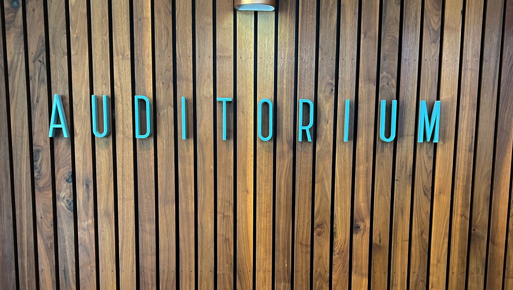 Blue letters spelling "Auditorium" on wood wall.