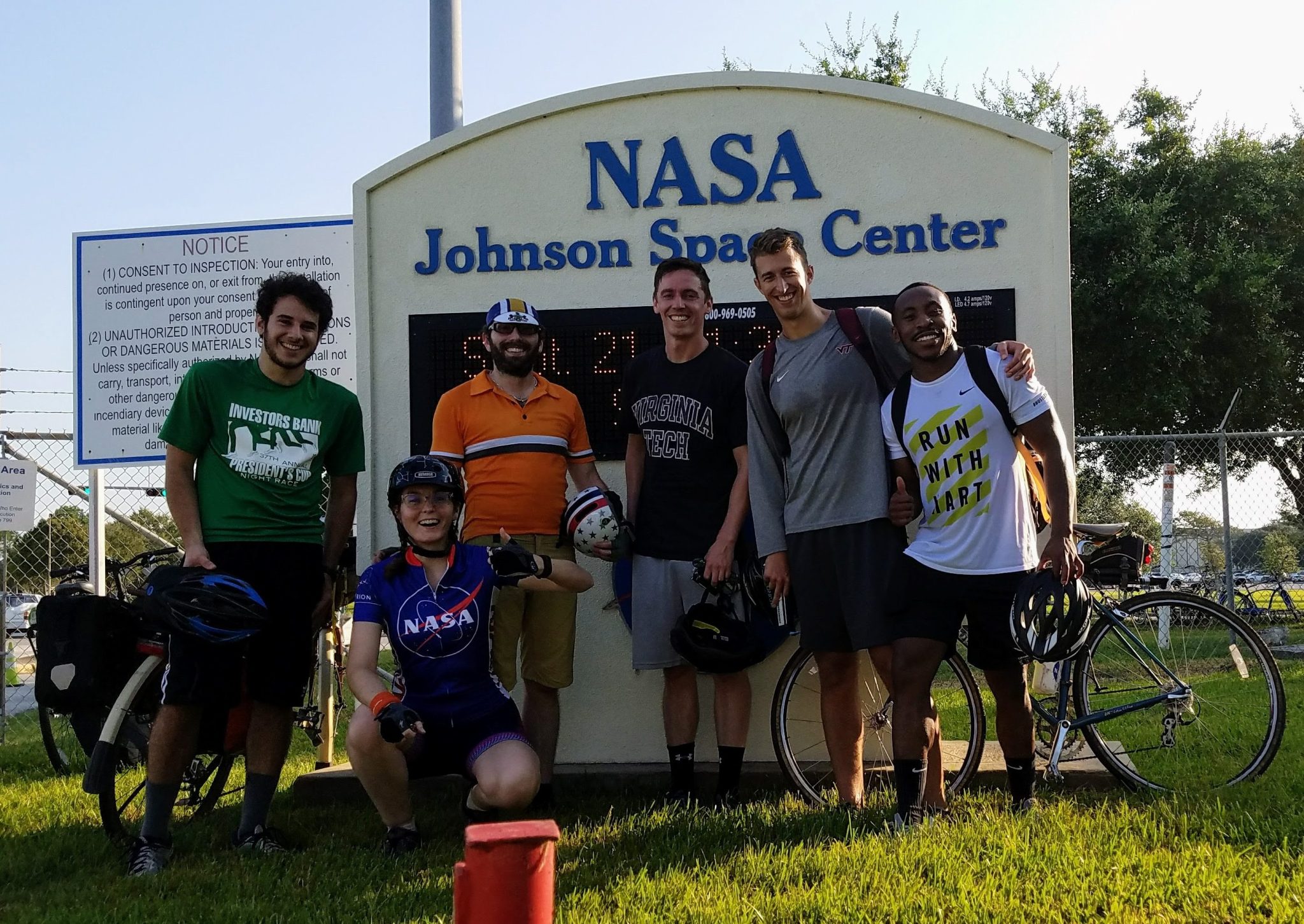 Six people stand outside on a sunny day in front of a NASA Johnson Space Center sign. They are all wearing workout apparel.