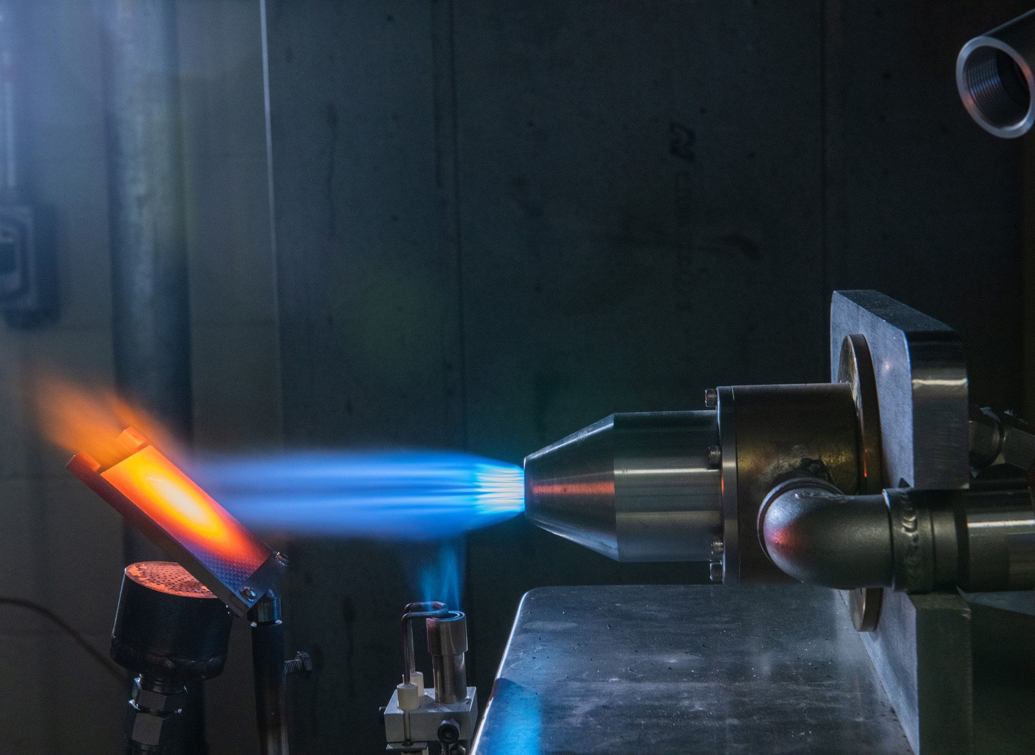 An orange-glowing metal plate is heated by a blue torch flame.