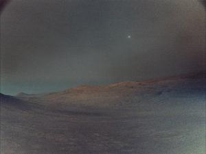 NASA's Perseverance rover captured this view of Deimos (the brightest spot in the sky), the smaller of Mars two moons, shining in the sky at 4:27 a.m. local time on March 1, 2025. The low light makes the view hazy, and the sky and ground both have a gray tint. In the distance, the crest of a crater shows Mars' signature rusty red color.