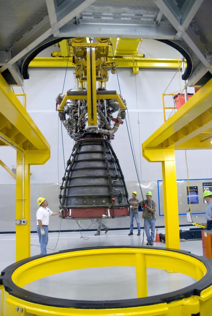 Three workers move a space shuttle main engine into place at an engine assembly facility