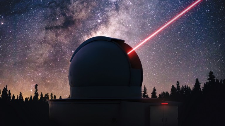 An artistic rendering of a circular ground station on Earth, shaded with shadows. The ground station sits in front of a row of shadowed pine trees and a bright night sky full of colorful stars. A red beam is shown transmitted from the ground station up to the upper right corner and out of frame, representing laser communications.