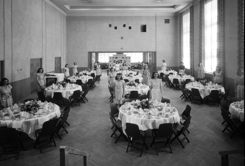Women standing by tables in auditorium.