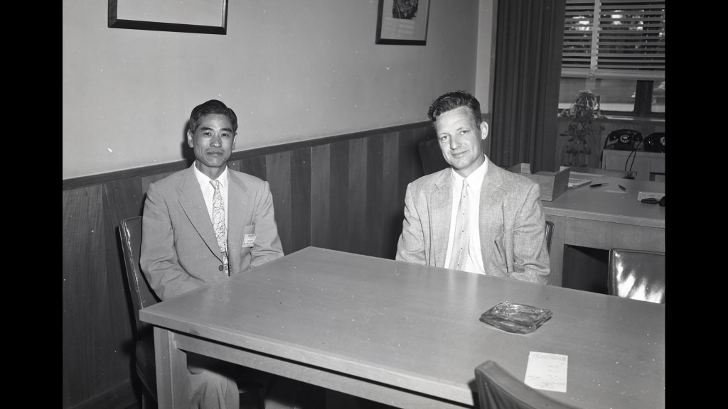Two men sitting at table in office.