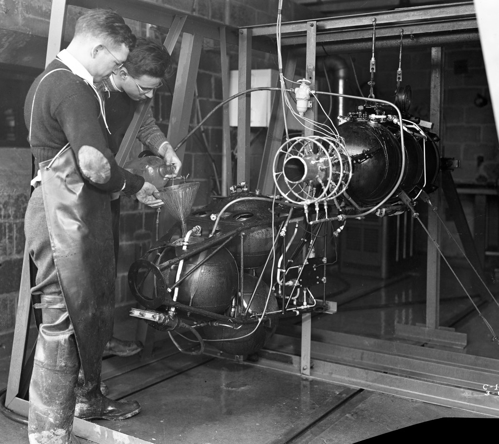 Two men pour fuel into engine.