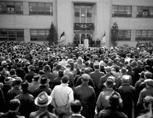 Group of people outside building listing to speaker.
