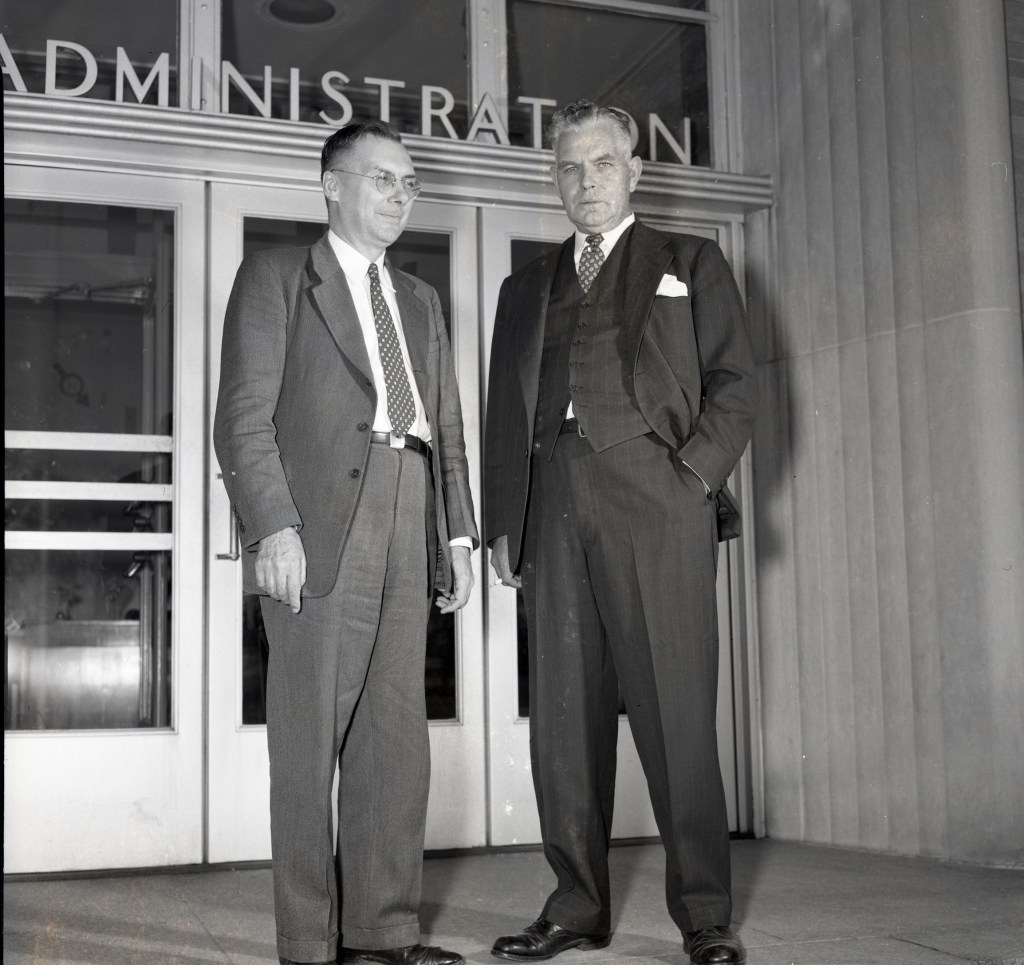 Two men standing outside building entrance.