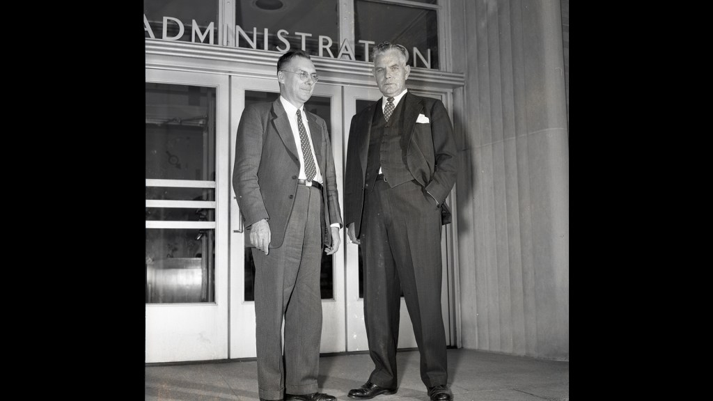 Two men standing outside building entrance.