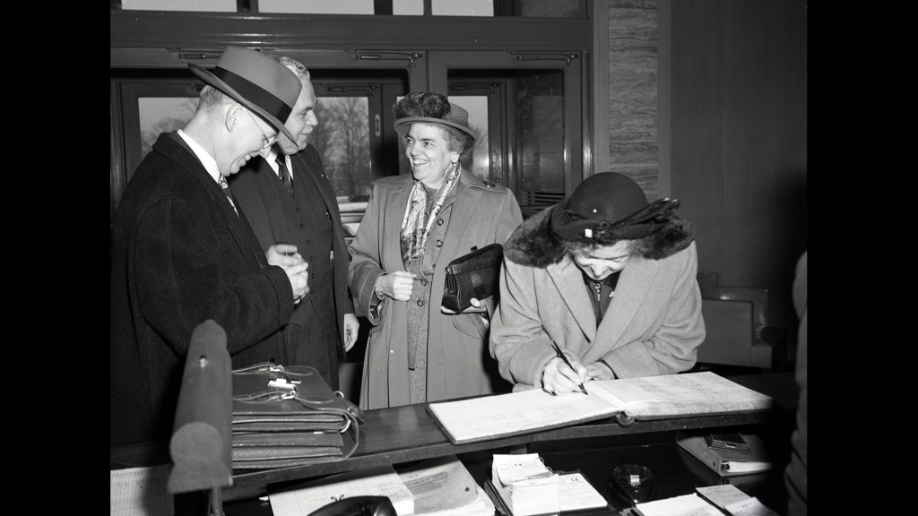 Women signing guestbook at lobby desk.