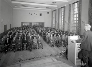 Man speaking to auditorium from podium.