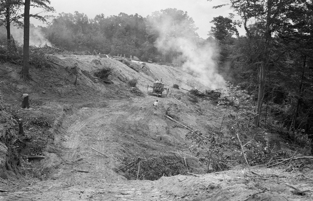 Bulldozer knocks down trees in wooded area.