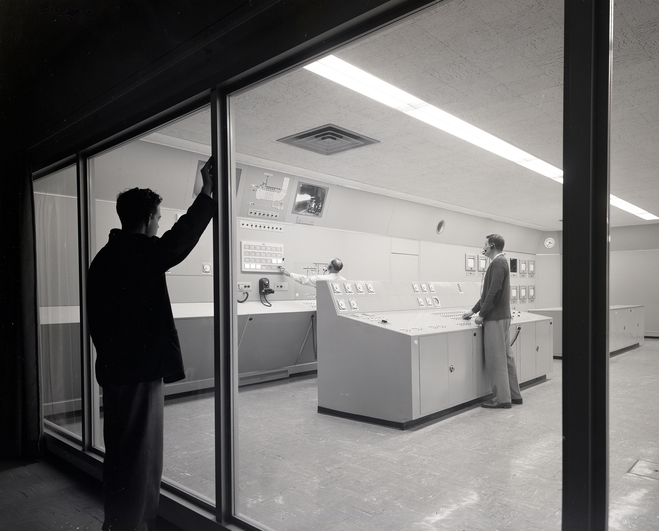 Man watches from outside two test operators in control room