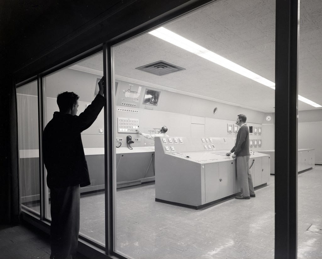 Man watches from outside two test operators in control room