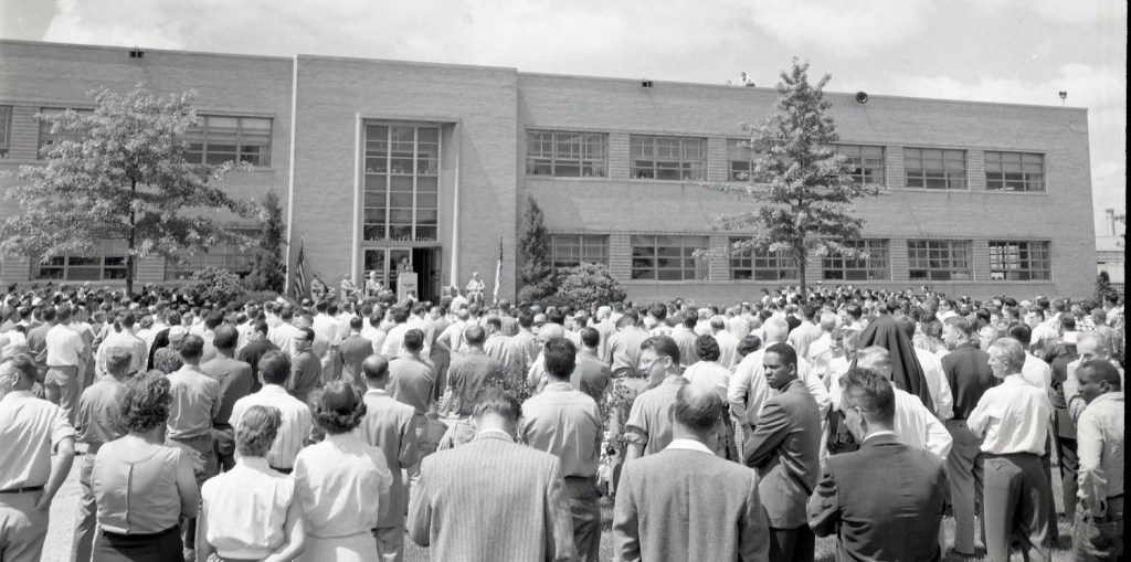 Group of people outside building listing to speaker.