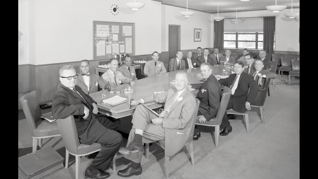Group of men seated at conference table.