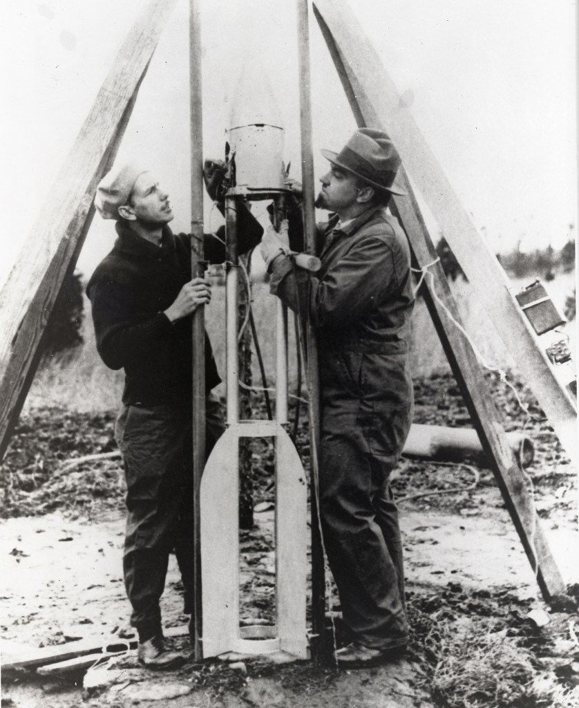 Two men holding small rocket.