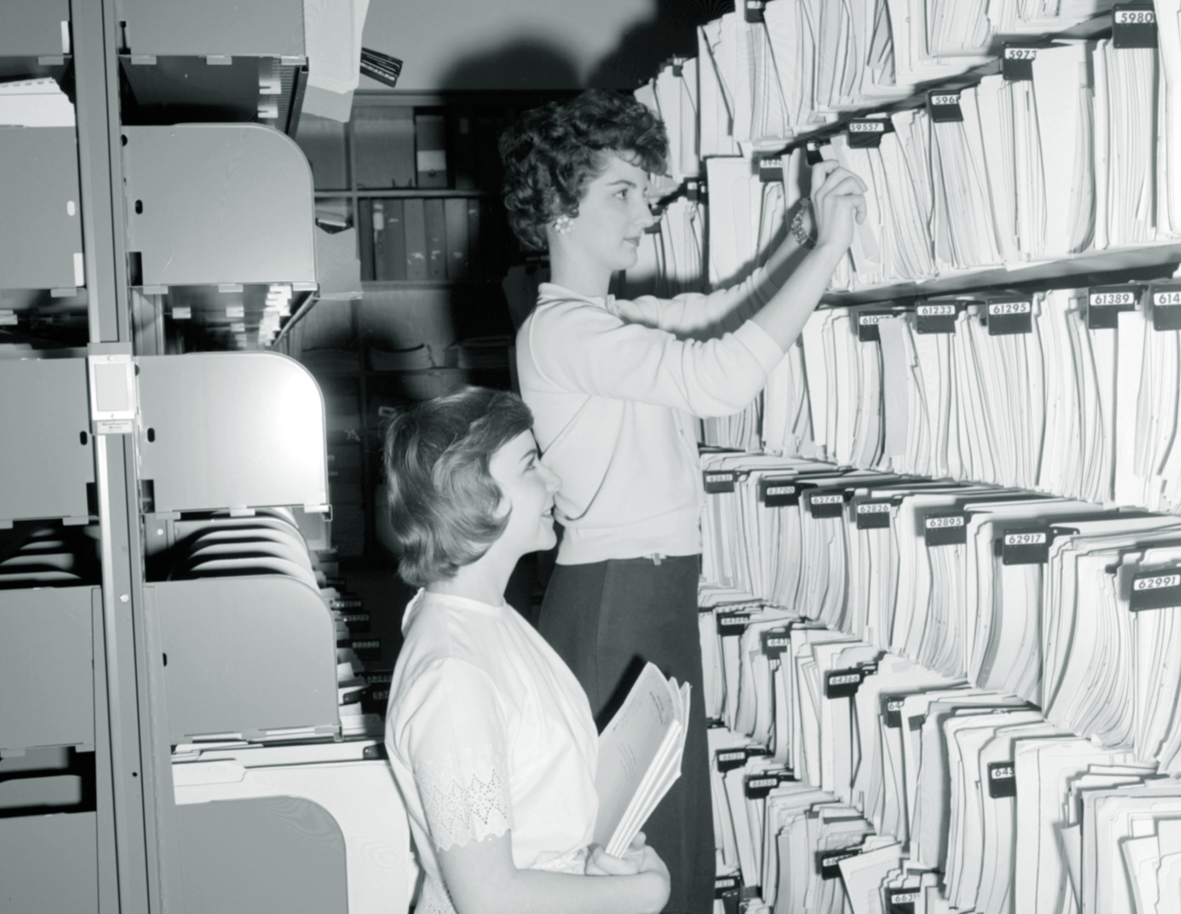 Two women pulling documents from a shelf.