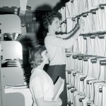Two women pulling documents from a shelf.