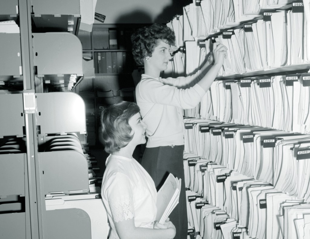 Two women pulling documents from a shelf.