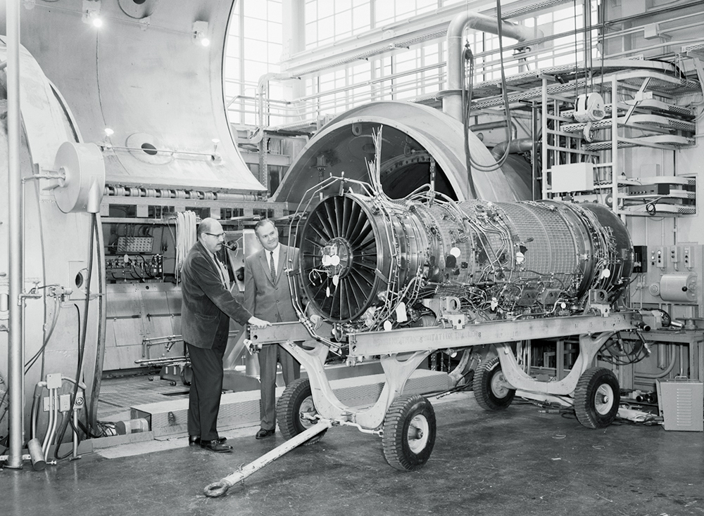 Men examine aircraft engine on cart.