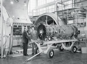 Men examine aircraft engine on cart.