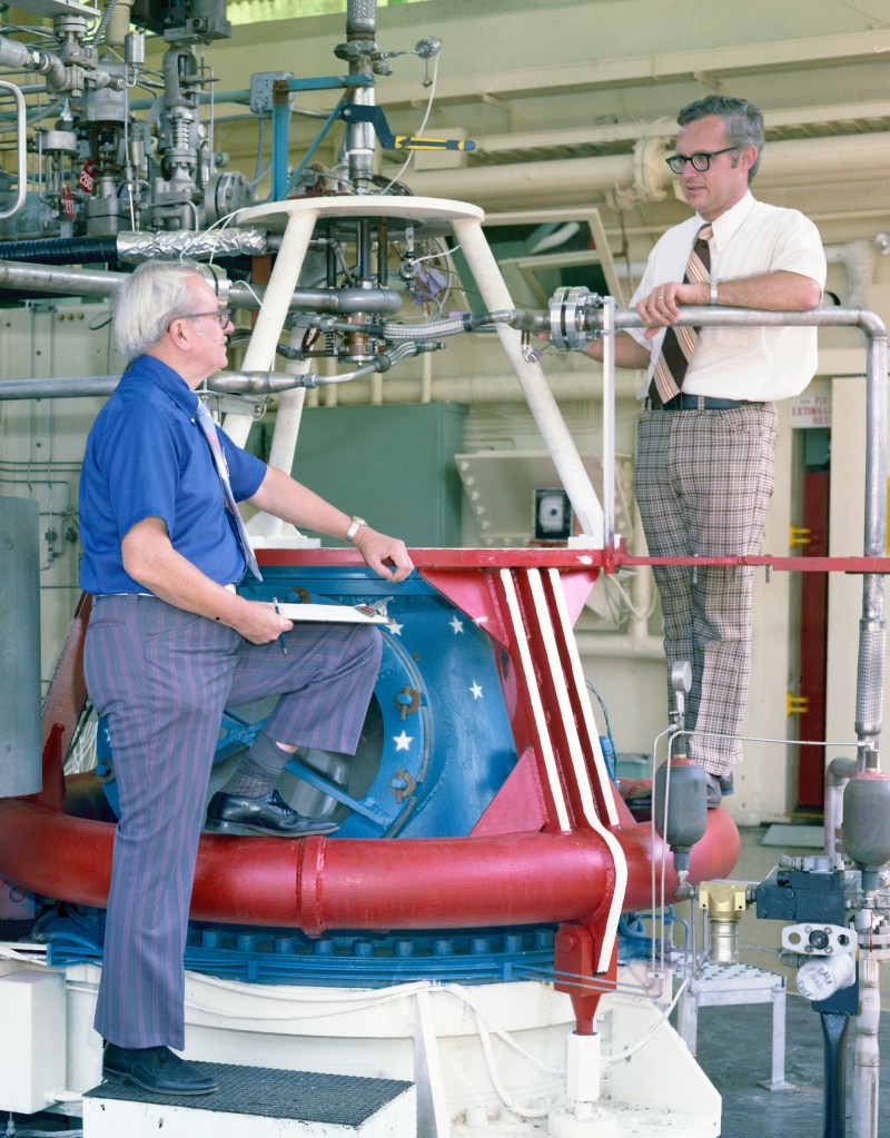 Two men standing at rocket stand.