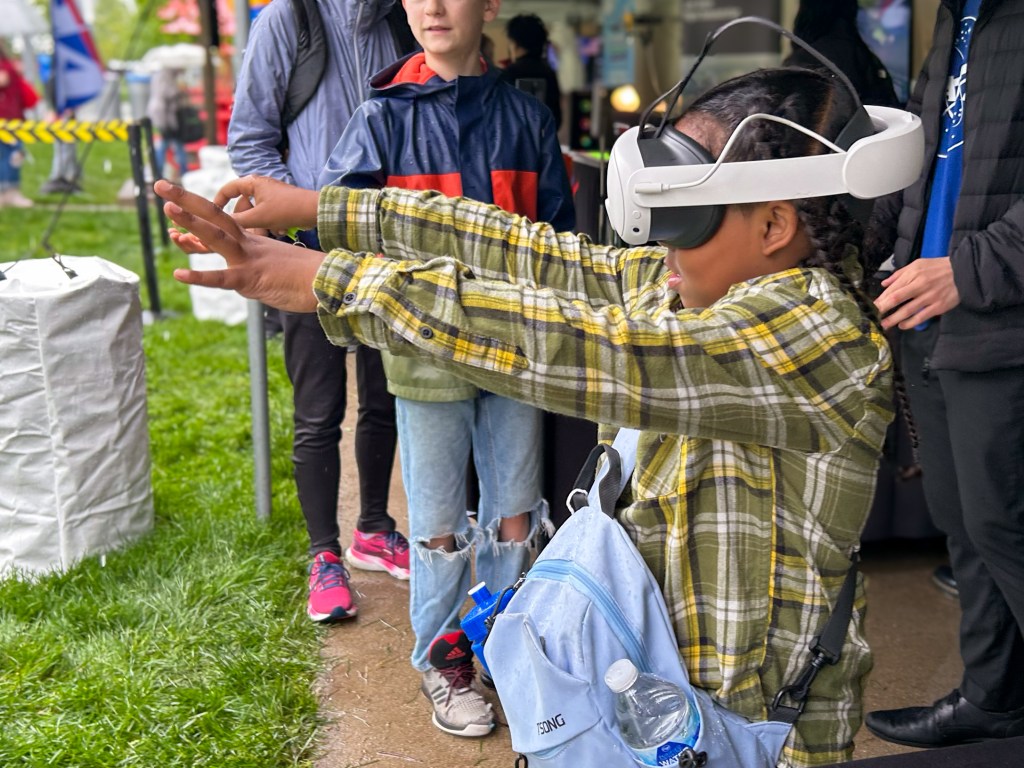 A girl wearing a virtual reality headset reaches her hands out in front of her to view objects through the headset.