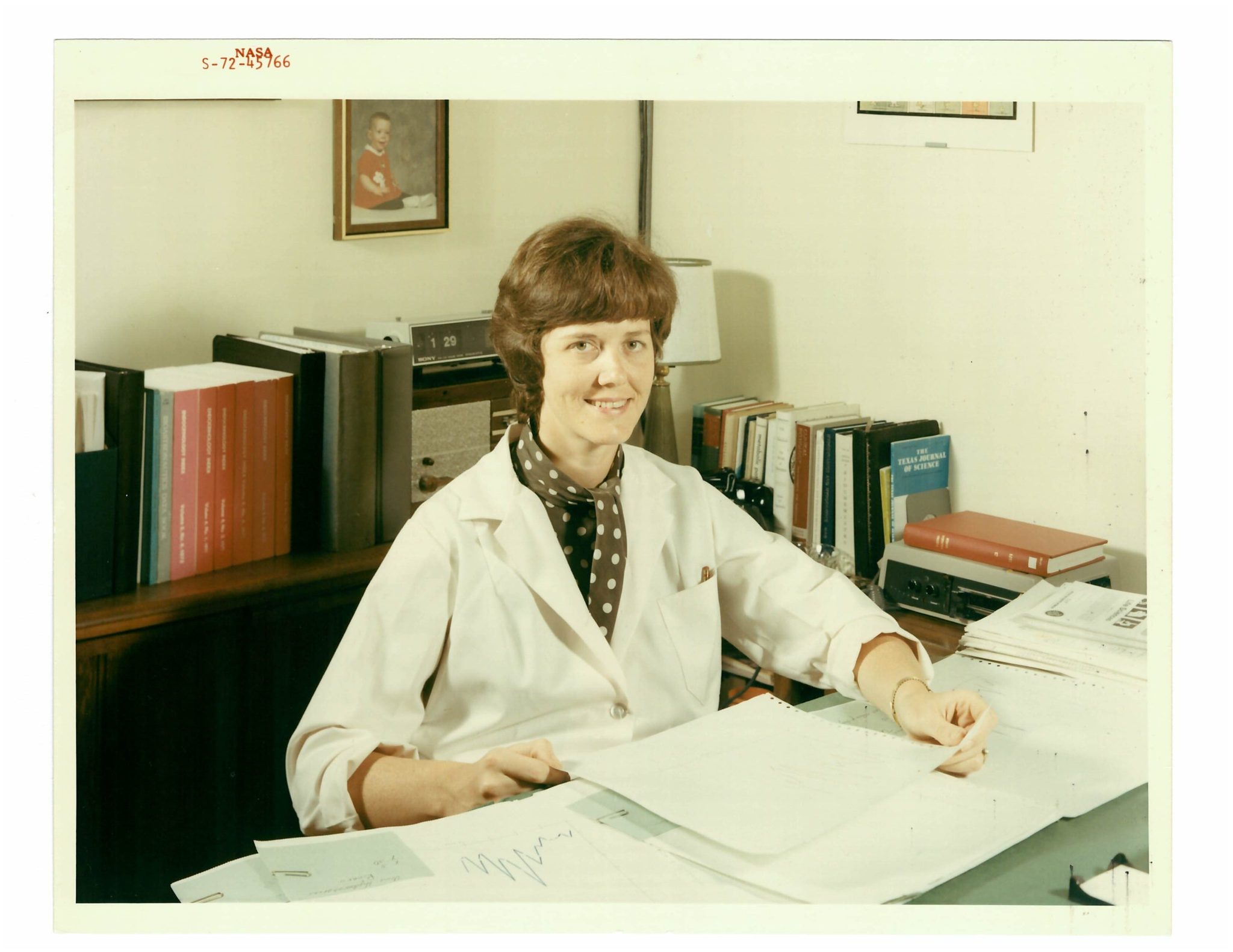 Portrait of Carolyn Huntoon wearing a lab coat and sitting at her desk.