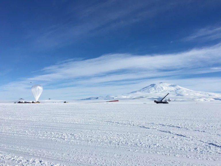 Balloon inflated in distance on snowy ground.