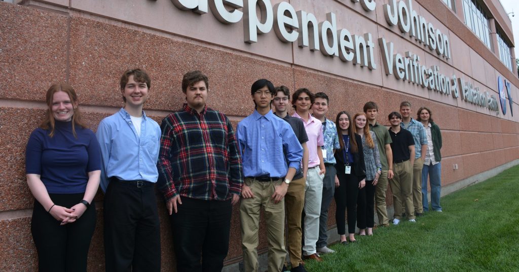 Thirteen high school and college interns standing in front of a building and smiling.
