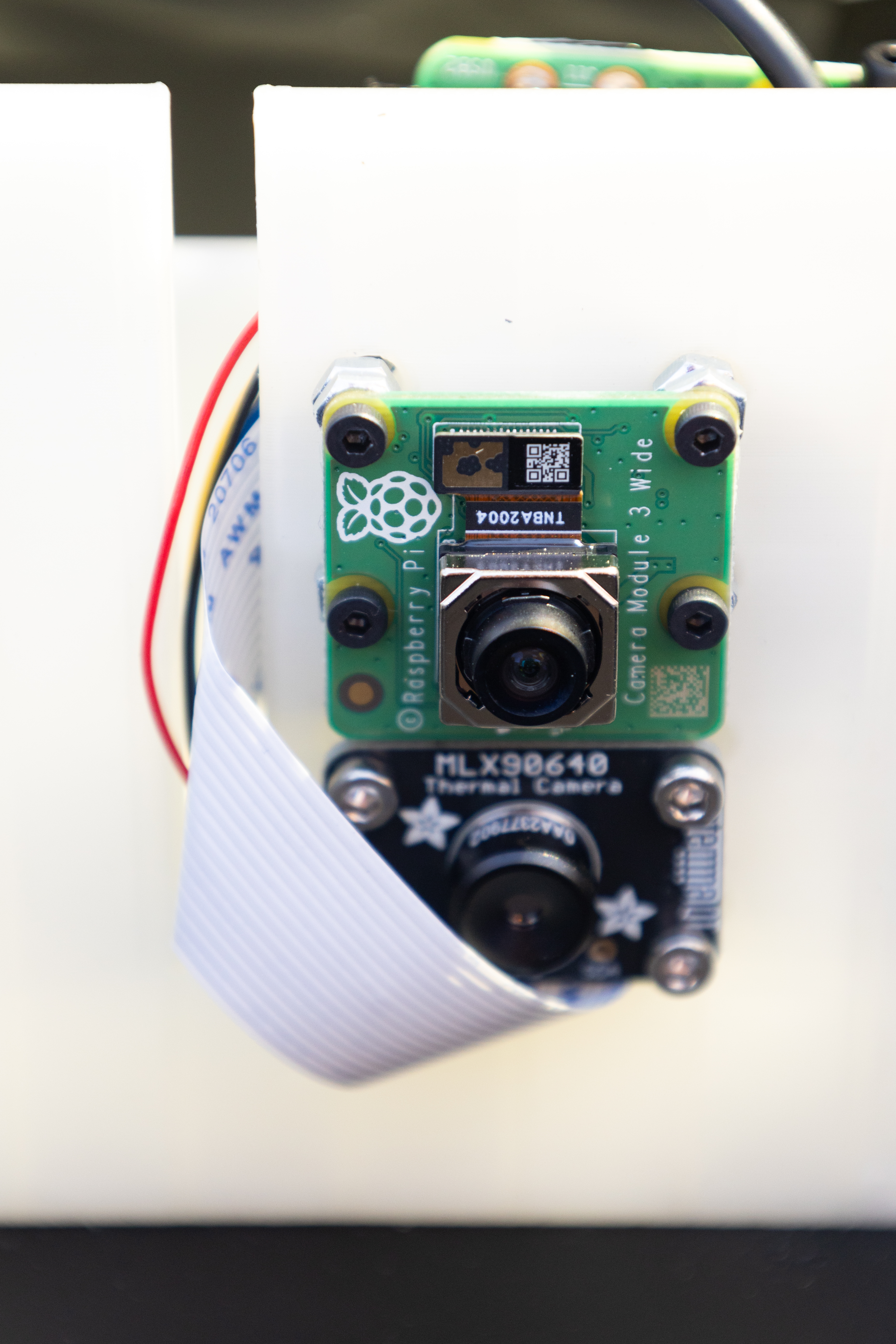 Two tiny camera lenses are mounted on a piece of white plastic, with a small red wire coming out the side.
