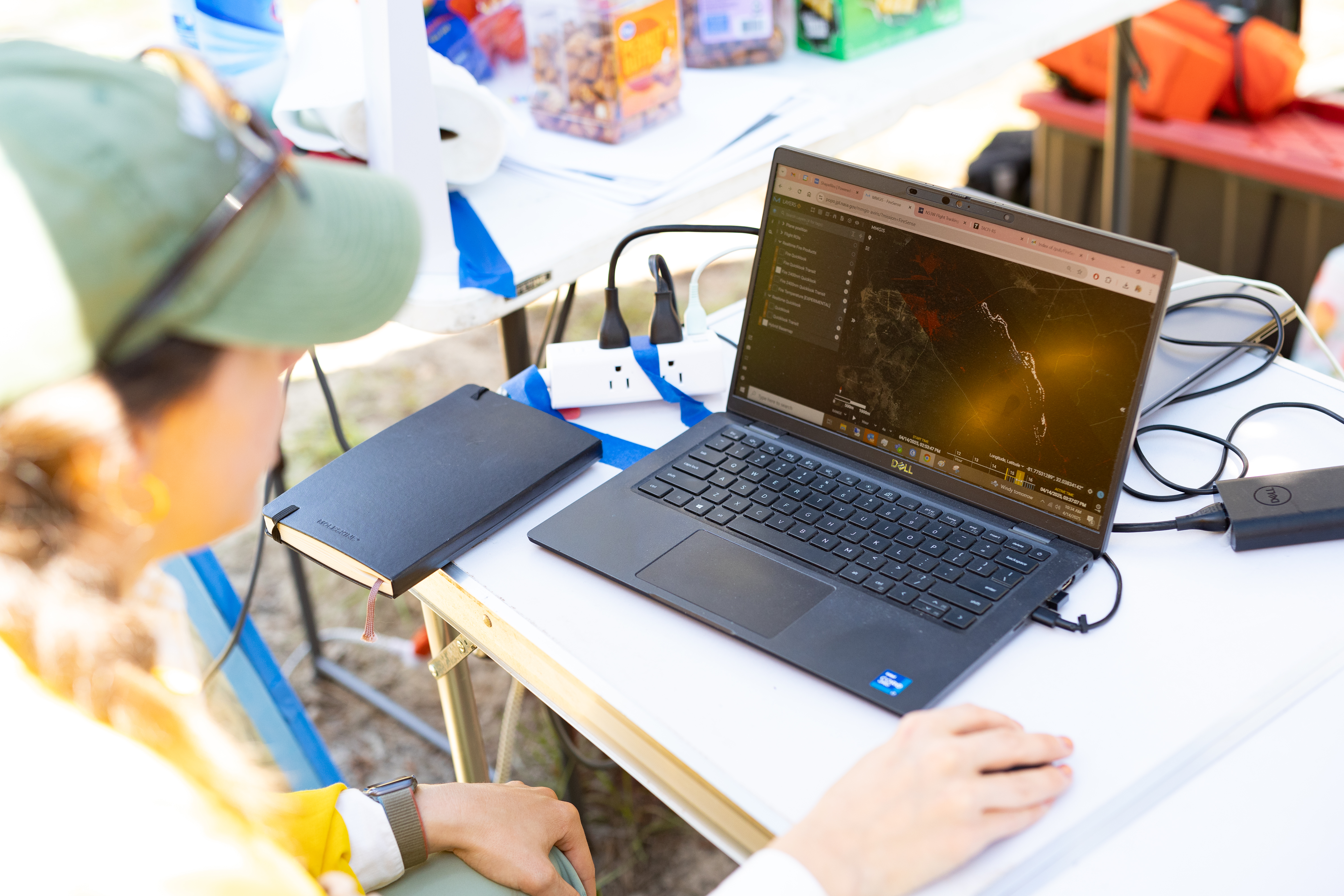 A scientist looks at a data visualization, white spots on a black background, on a laptop sitting on a on white table that also holds a notebook and computer cords.