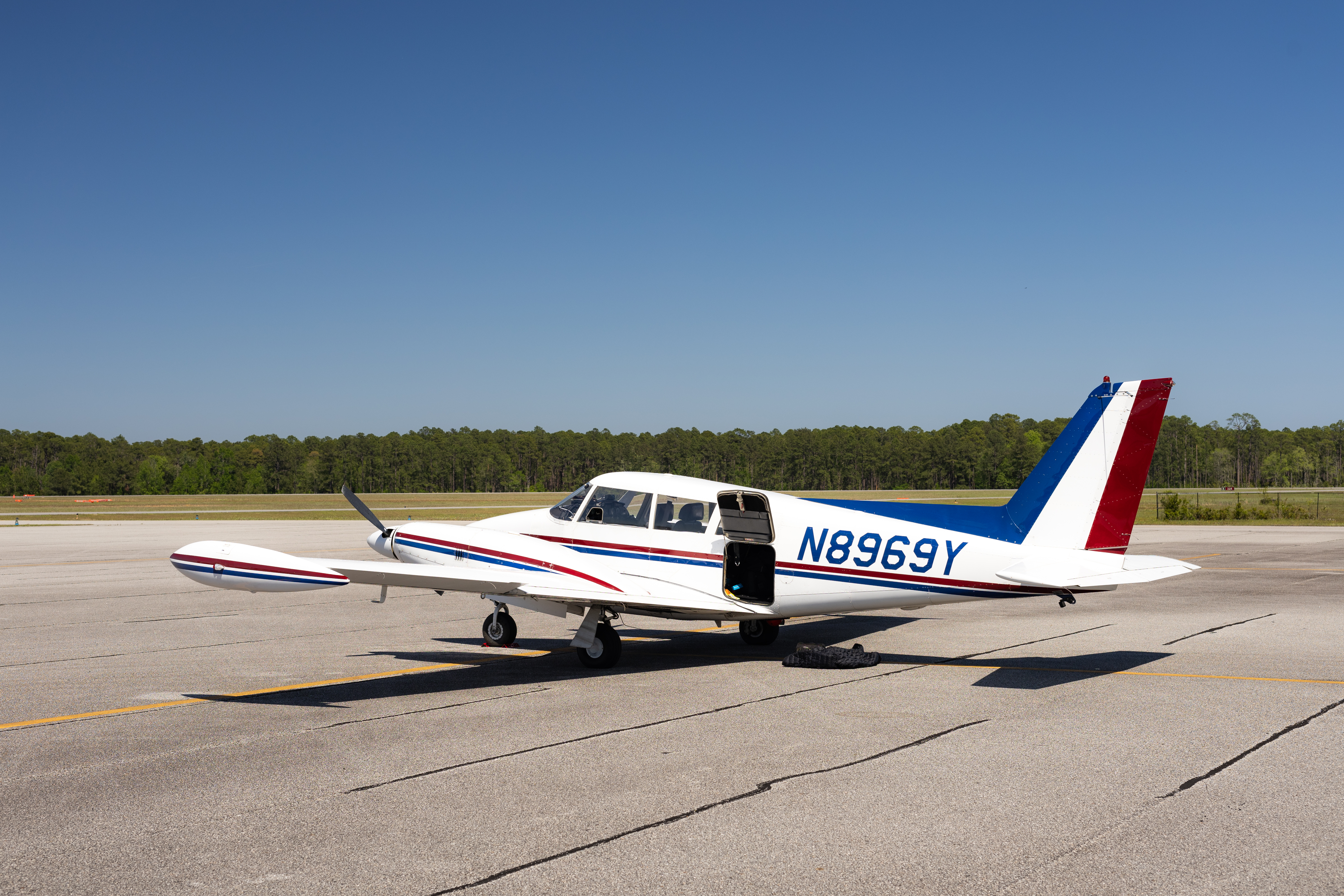 A small white aircraft sits on a gray airplane tarmac, with blue sky in the background.