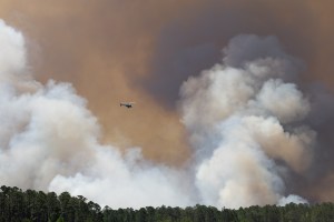 Helicopter flies in front of smokey clouds above a forest.