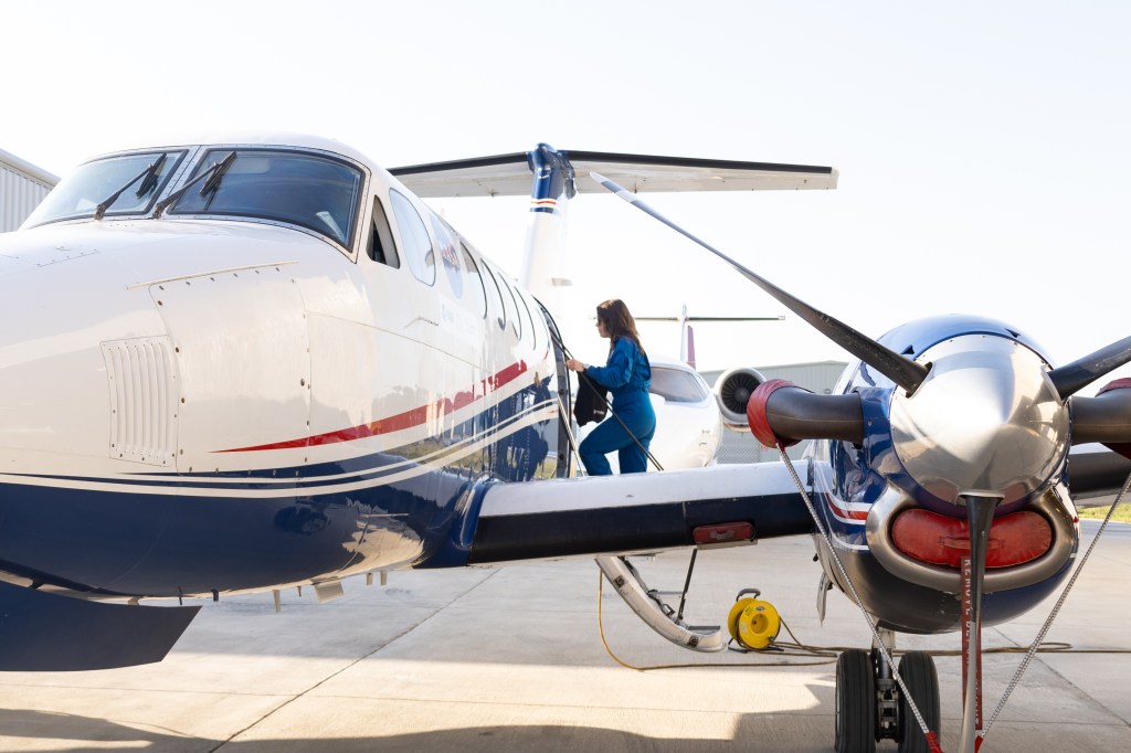 A woman in a blue flight suit climbs a short staircase to board a white and blue NASA aircraft.