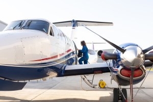 A woman in a blue flight suit climbs a short staircase to board a white and blue NASA aircraft.