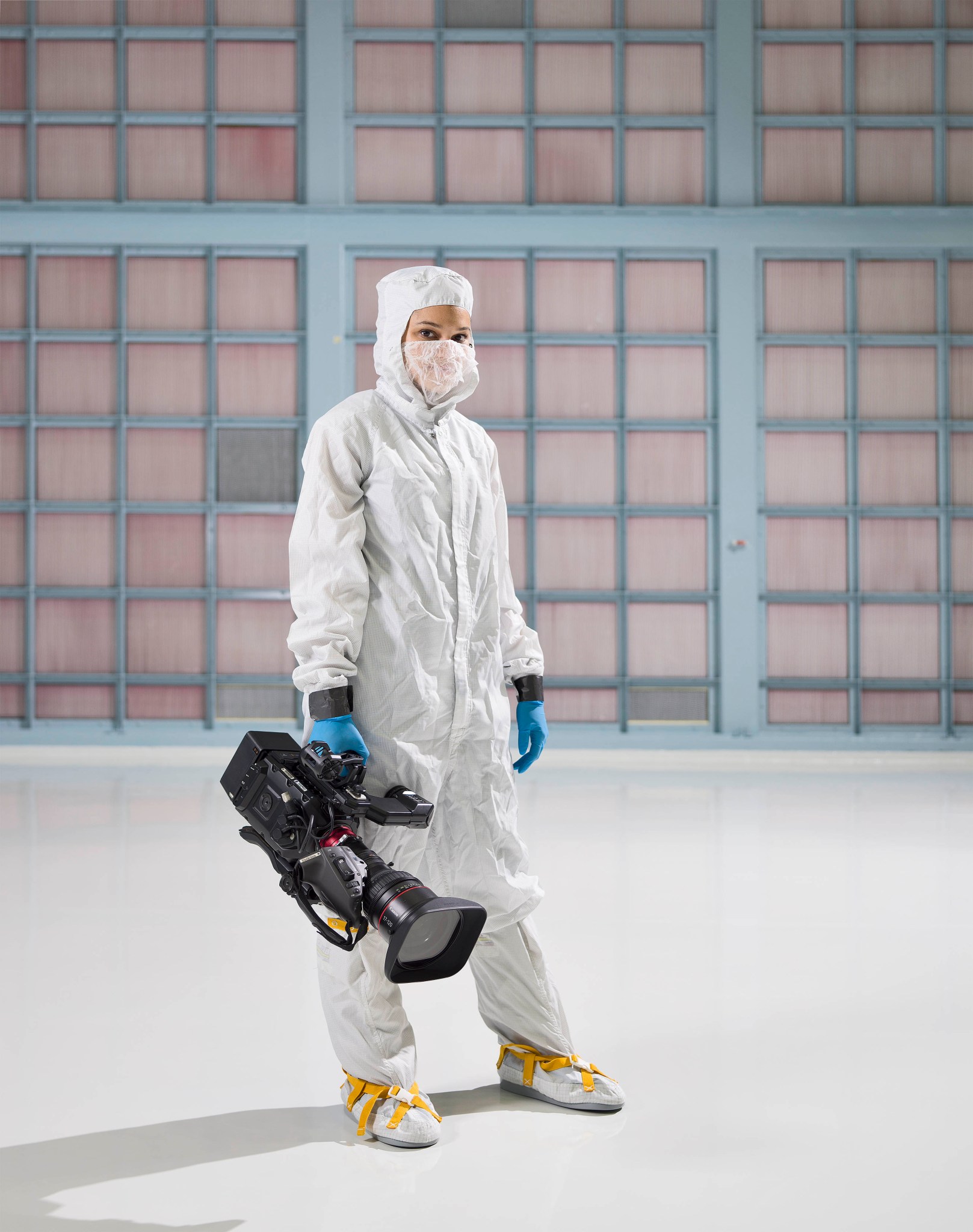 A photo of Sophia Roberts in a white bunny suit in the Goddard clean room holding a video camera