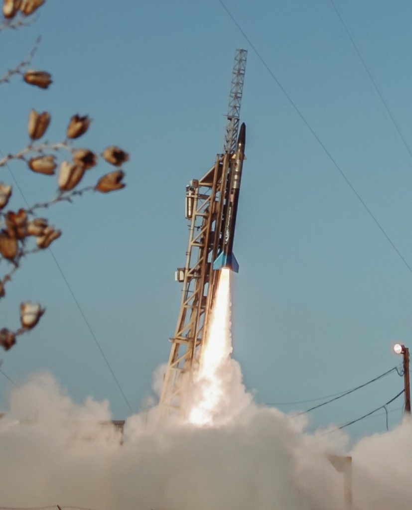 A rocket with flames and smoking billowing from its engine prepares to launch.