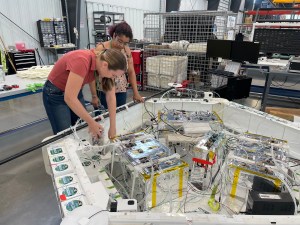 Two people bend over a large pentagon-shaped payload gondola, integrating experiments for a flight test.