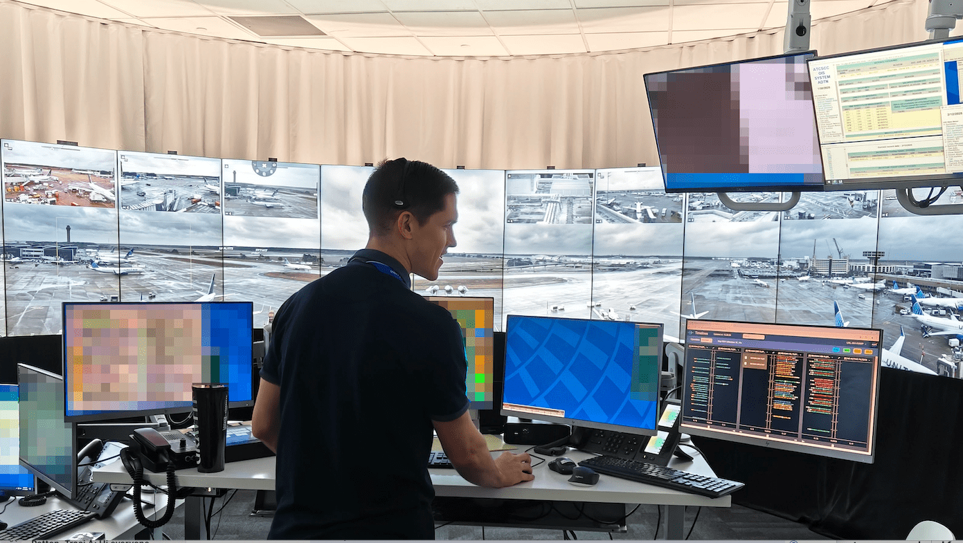 A man wearing a dark ship interacting with software while looking at multiple monitors.