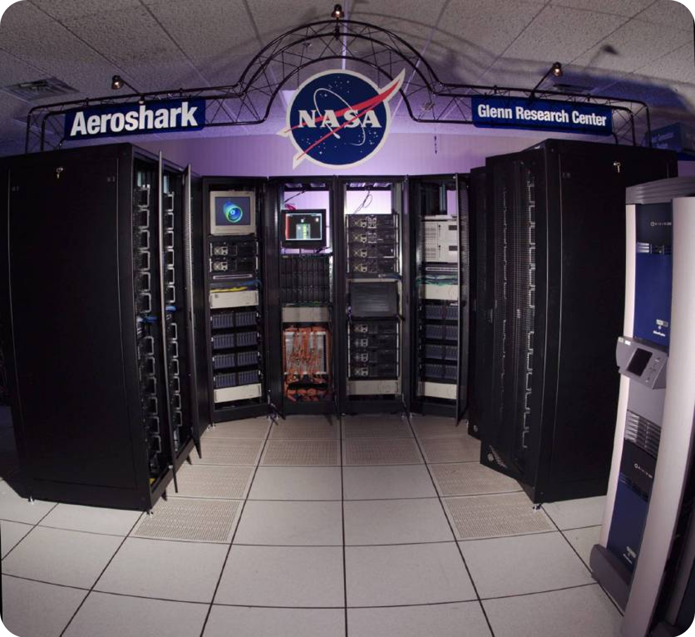 A small, dimly lit room contains tall rows of television screens stacked on top of one other.  An archway hangs from above the small section of computers reading: (from left to right) "Aeroshark", "NASA", "Glenn Research Center".
